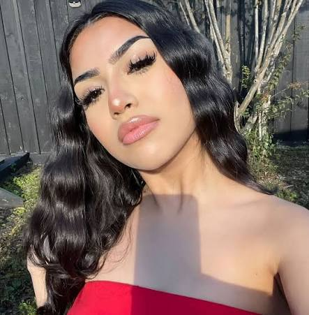 Outdoor beauty portrait of a woman with long, glossy waves and soft glam makeup, wearing a red strapless top and natural sunlight highlighting her features. wearing Herfa Maxwell beauty luxury strip lashes